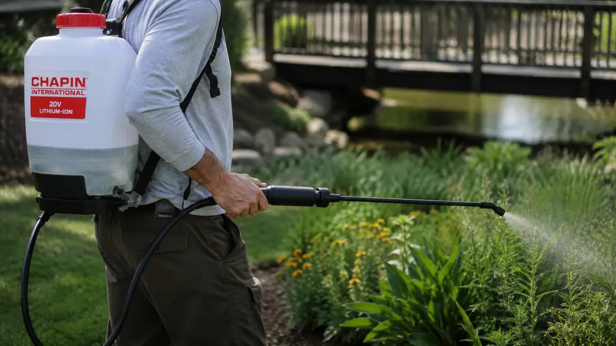 Close-up of a hand pumping the sprayer's left-side pump arm while spraying along a fence line